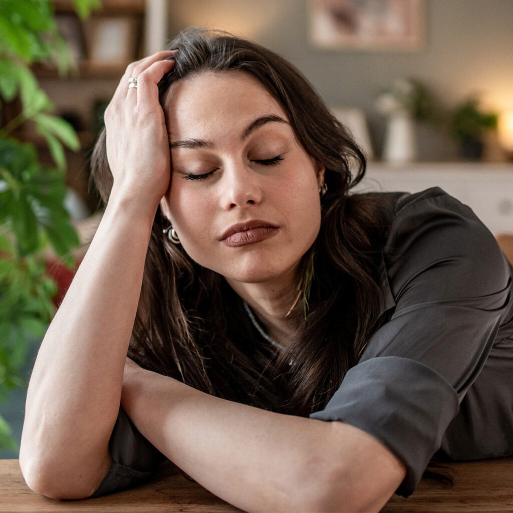 A tired woman leans her head on her hand with eyes closed.