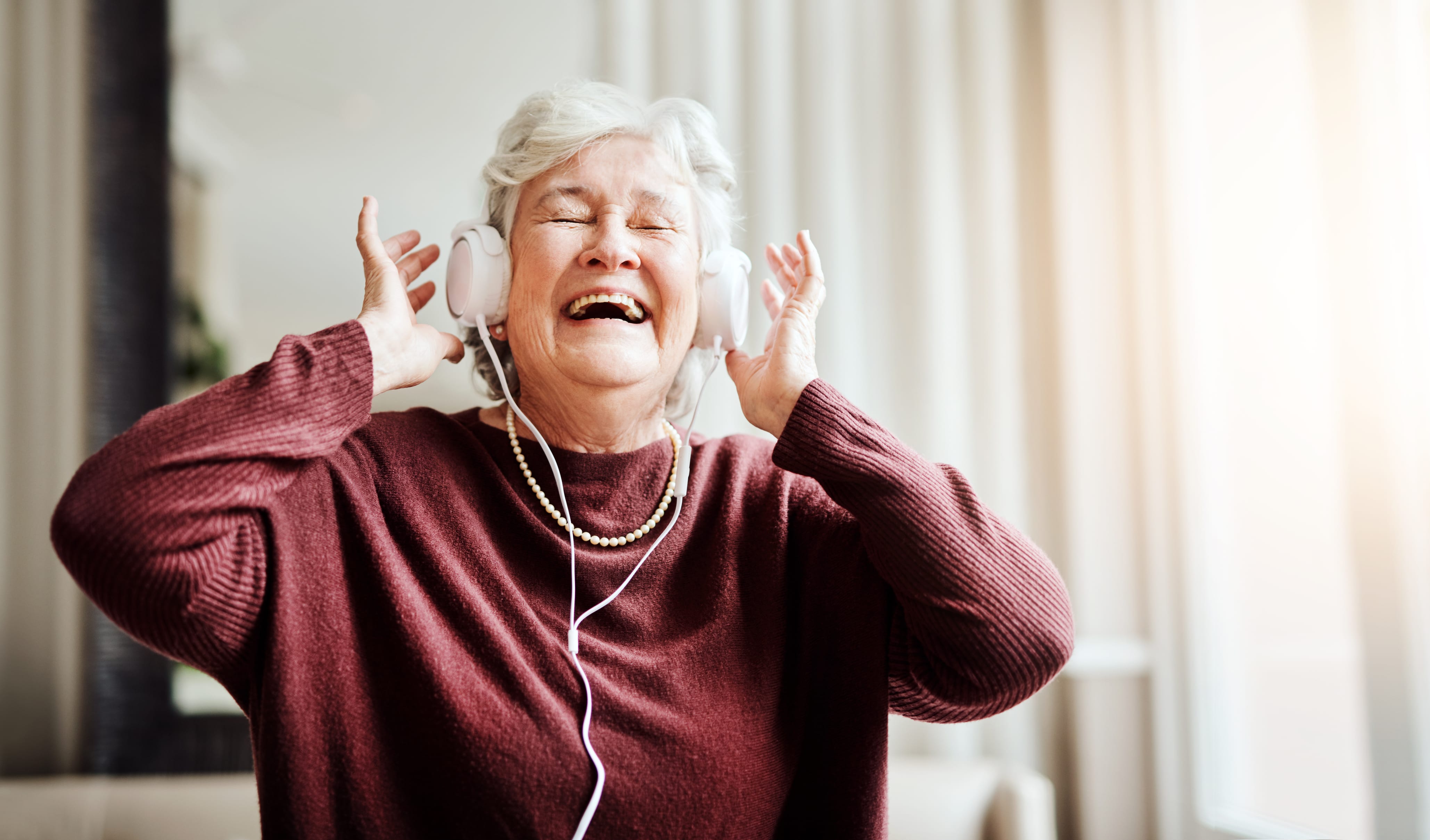 Shot of happy senior woman listening to music with headphones at a retirement home