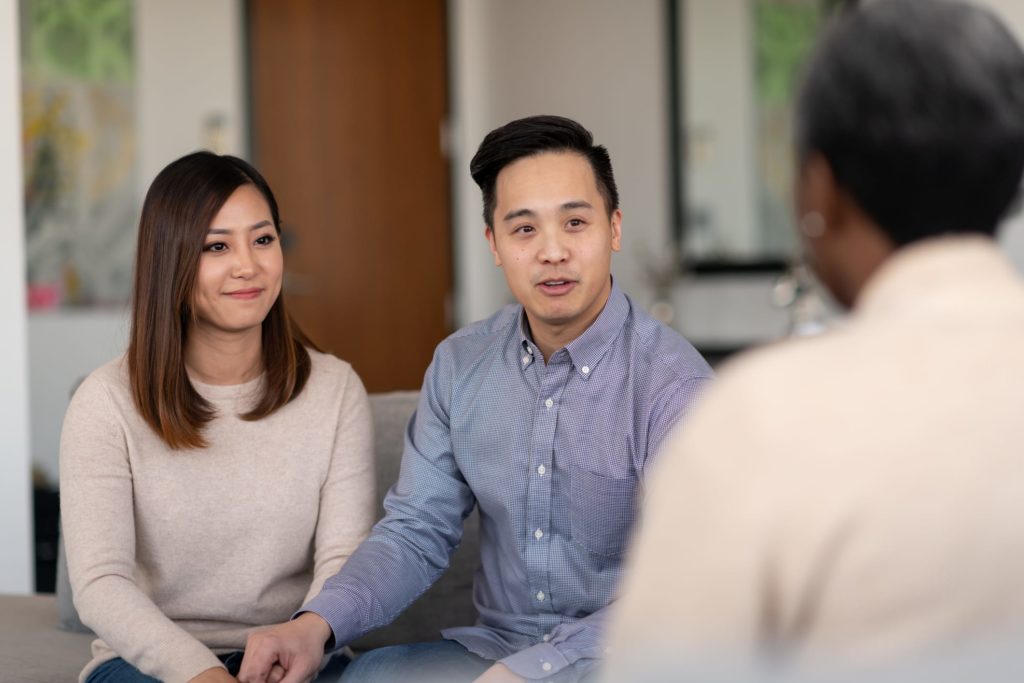An Asian married couple talks to a therapist together about their life. They are attentive and focused on making their marriage counseling.