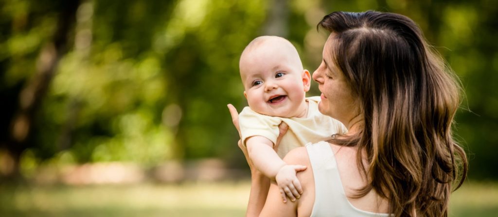 Happy mother holding her baby on hands outdoor in nature