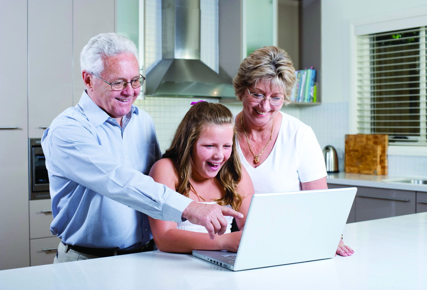 Two older parents and their daughter looking at a laptop in a kitchen