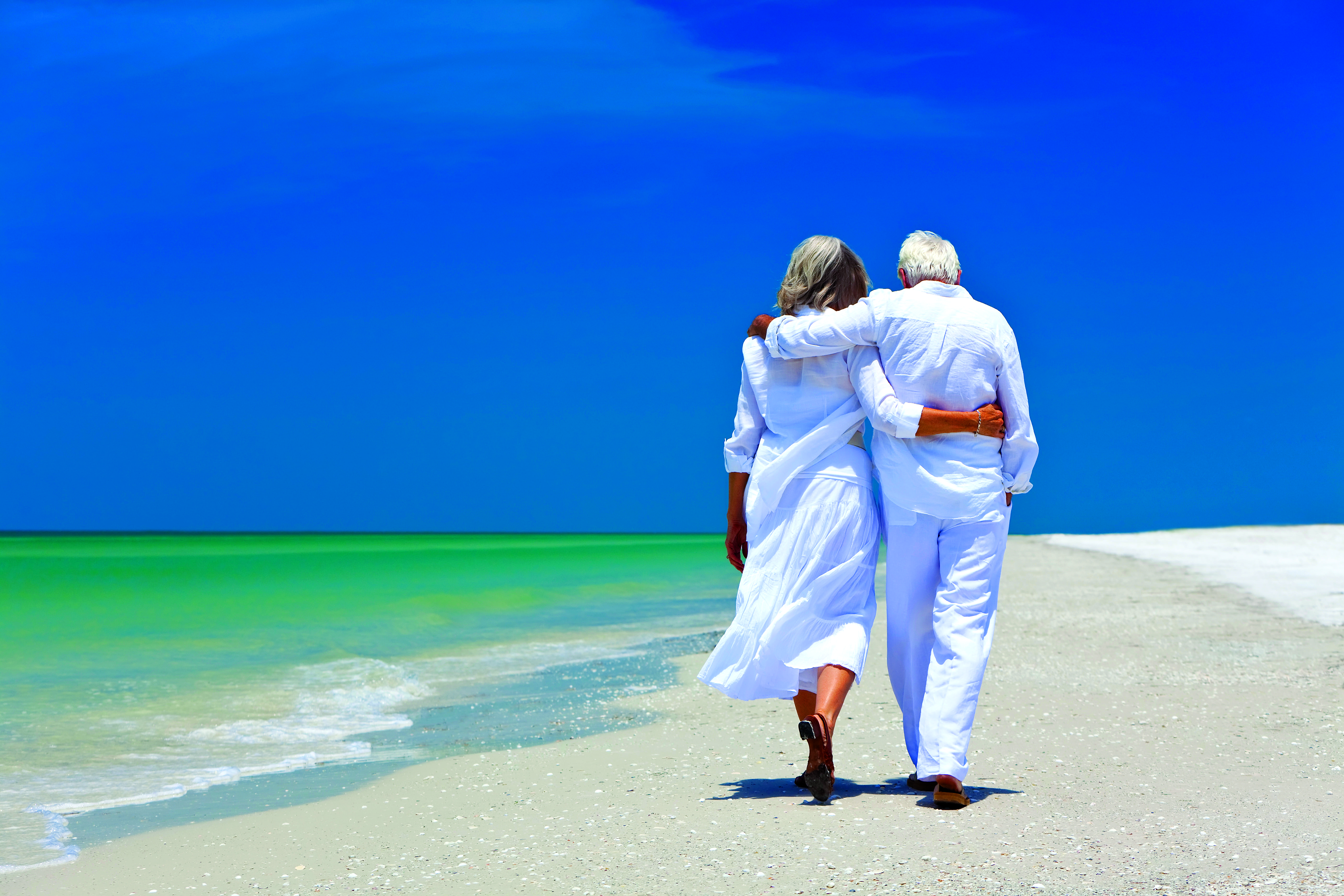 Man and woman walking down beautiful beach together arm in arm