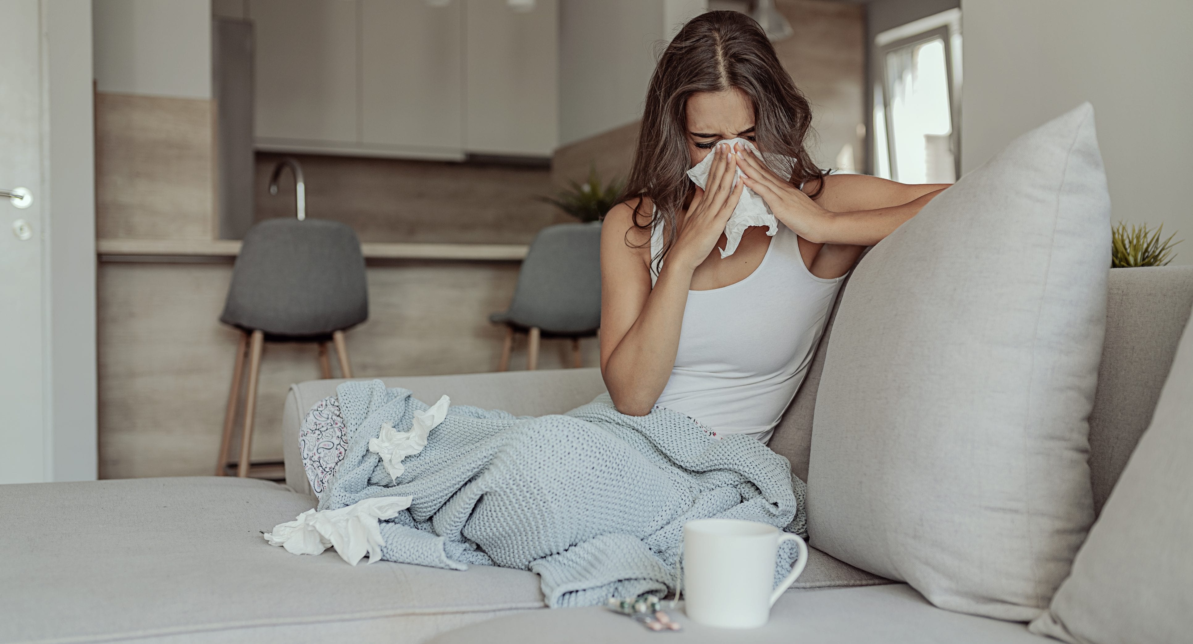 Sick Woman Covered With a Blanket Lying in Bed With High Fever and a Flu, Resting at Living Room. She Is Exhausted and Suffering From Flu. Sick Woman With Runny Nose Lying in Bed. Girl Suffering From Cold Lying in Bed With Tissue Blowing Her Nose While Sitting on the Sofa