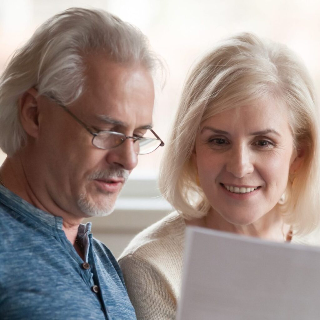 Happy old middle aged couple holding reading good news in document, smiling senior mature family excited by mail letter, checking paying domestic bills online on laptop, discussing budget planning