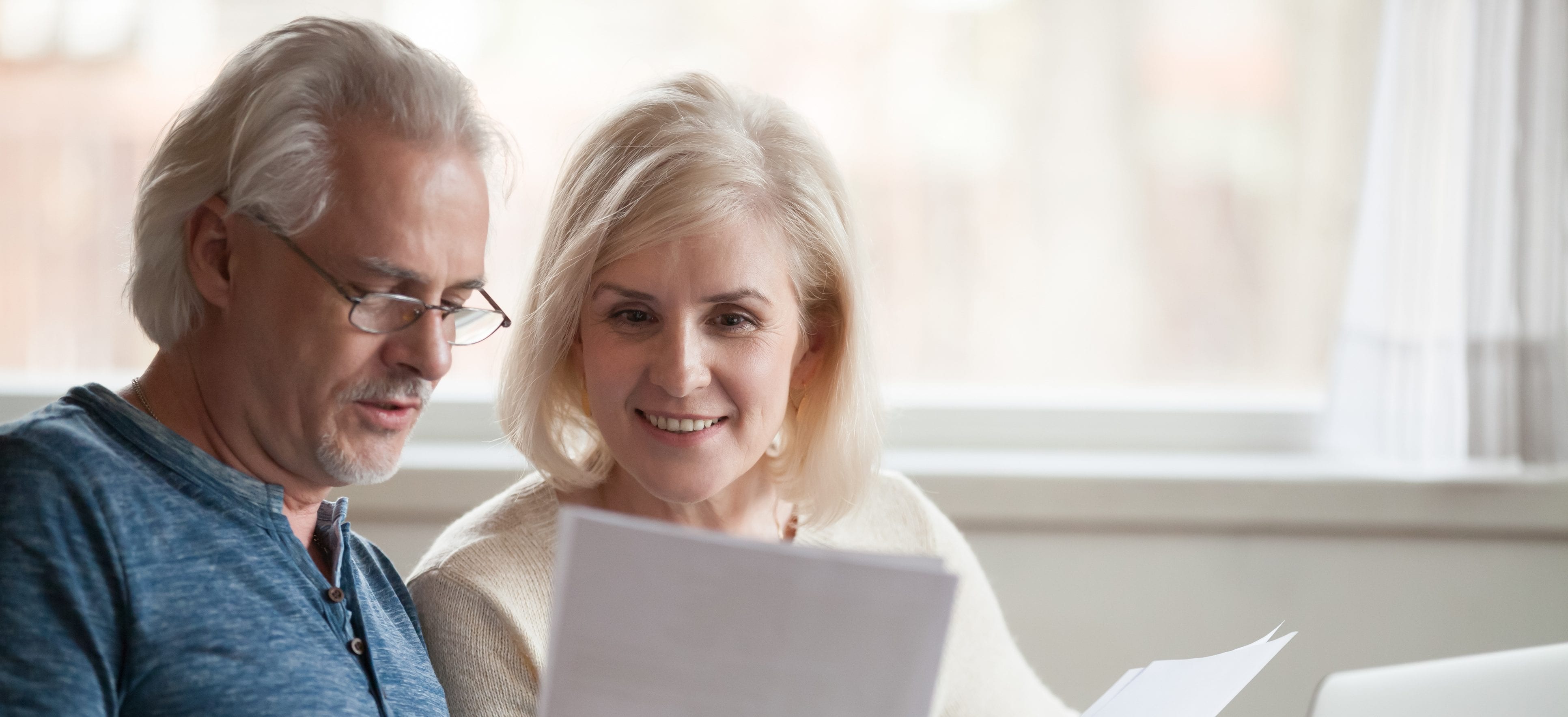 Happy old middle aged couple holding reading good news in document, smiling senior mature family excited by mail letter, checking paying domestic bills online on laptop, discussing budget planning