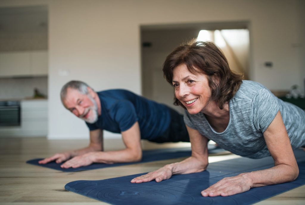 A happy senior couple indoors at home, doing power yoga on the floor.