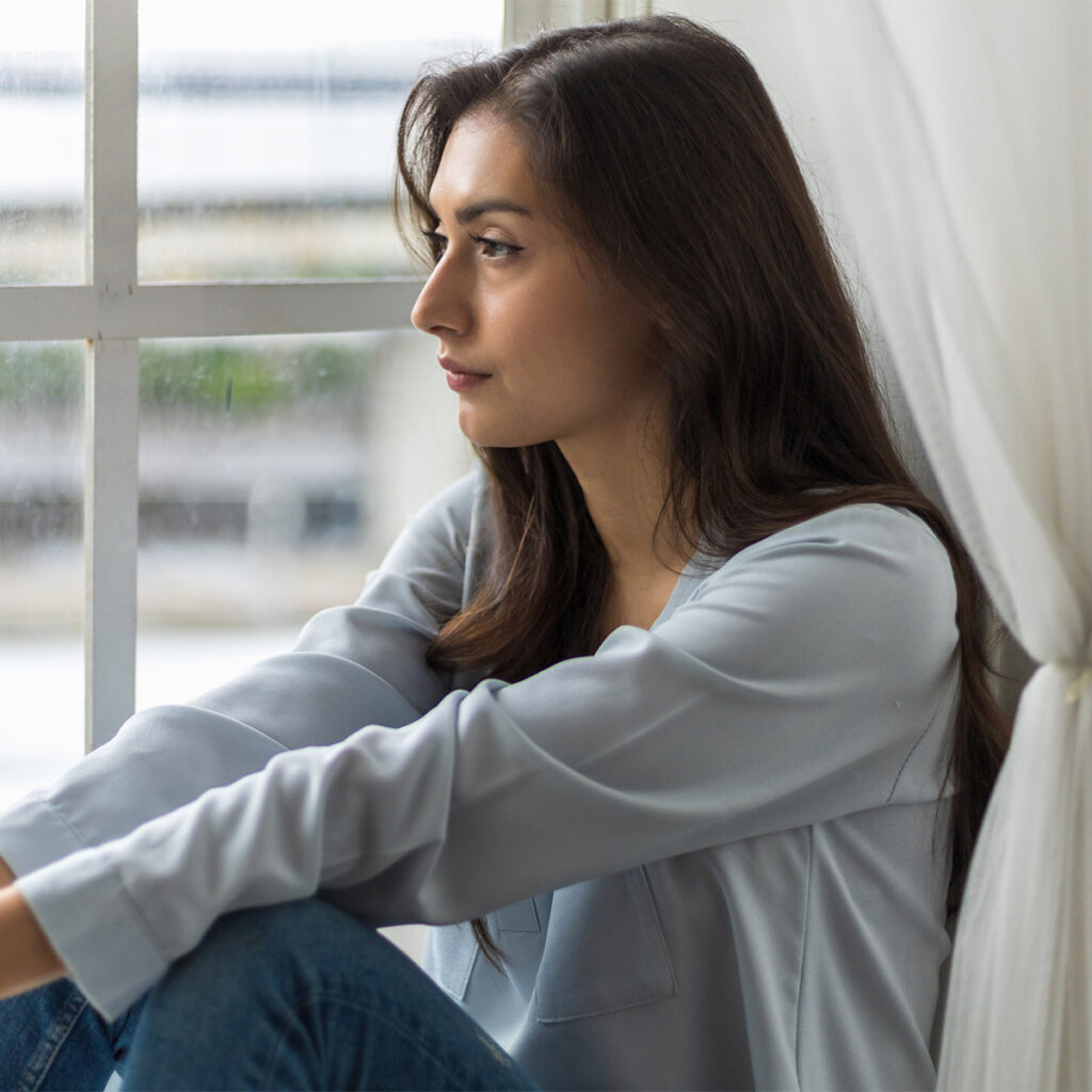 woman with mental illness looks out at dreary window