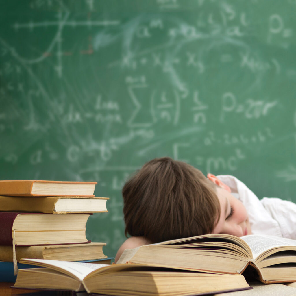 school boy sleeping on a desk filled with books