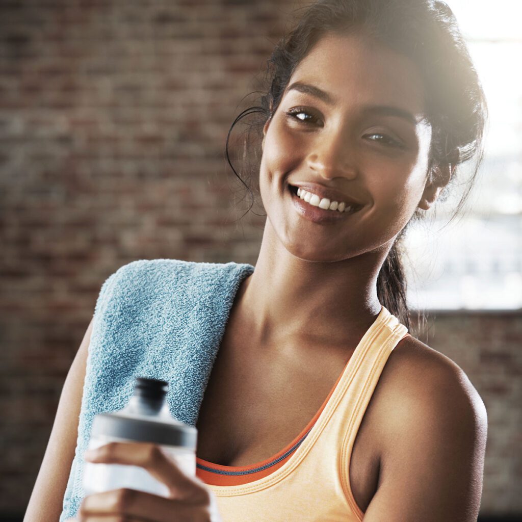 young smiling fit woman holding a water bottle with a towel on her shoulder