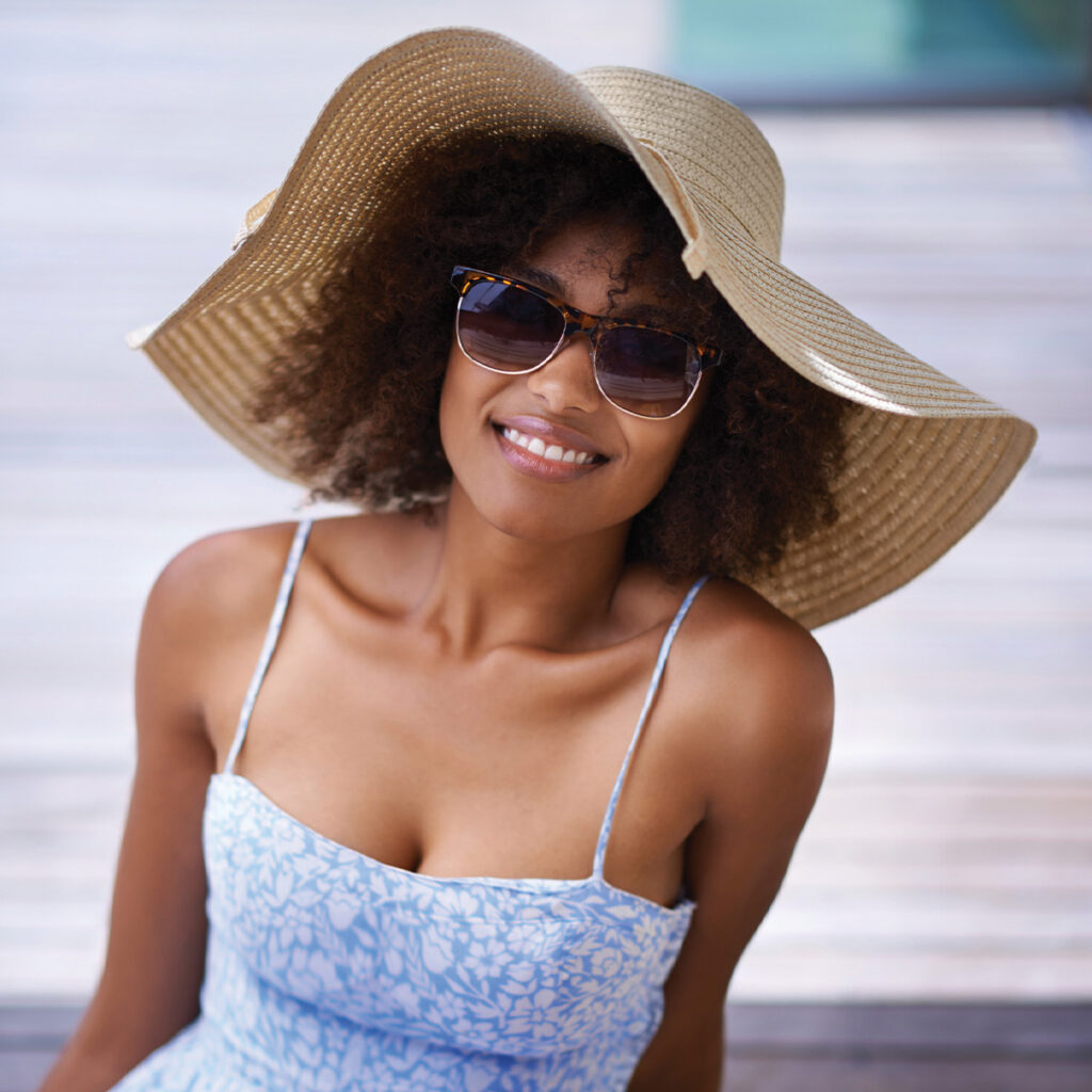 smiling woman with sun hat, sun dress, and sunglasses on