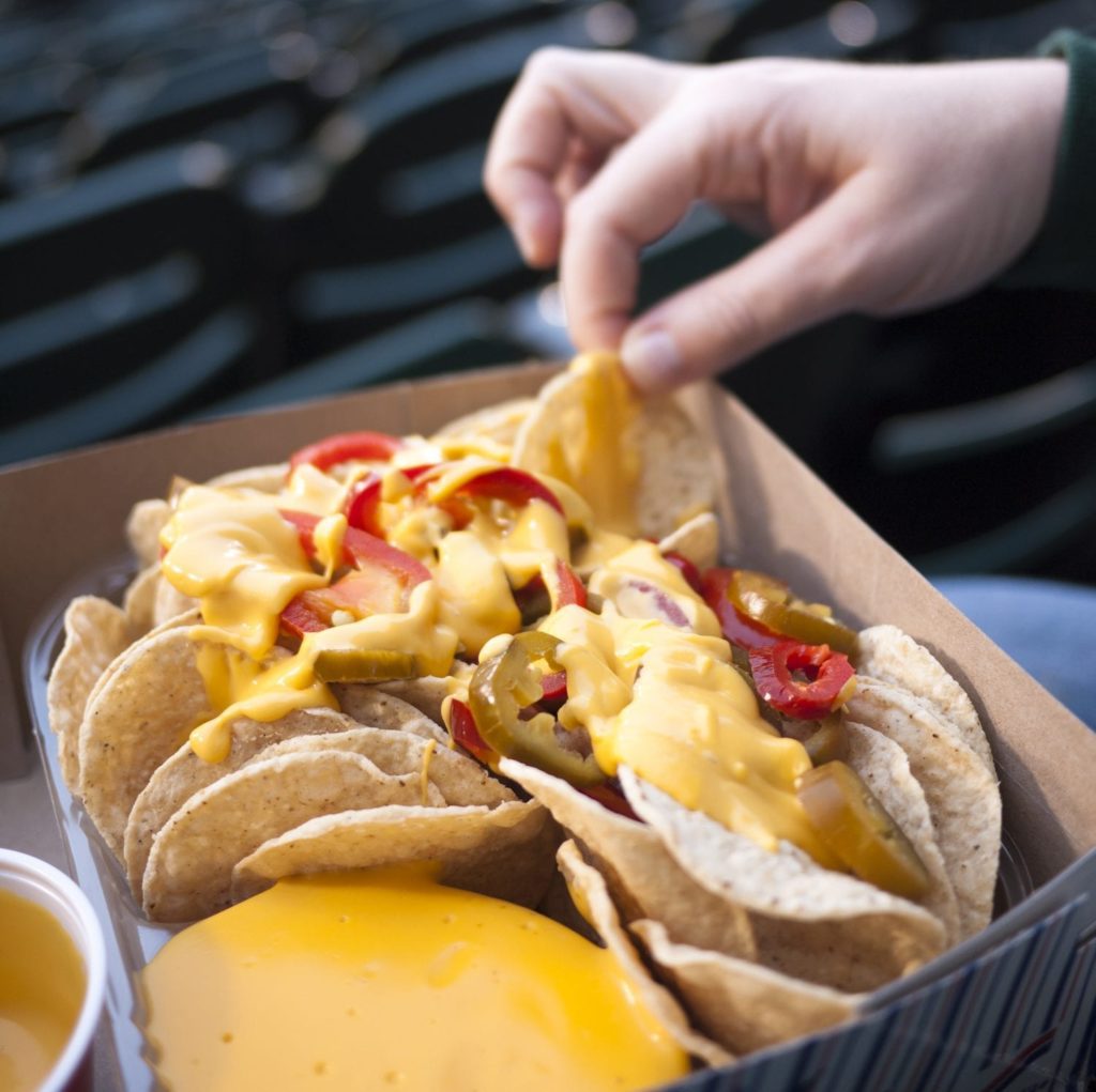 A person's hand picking up nacho chips at a baseball ballpark.