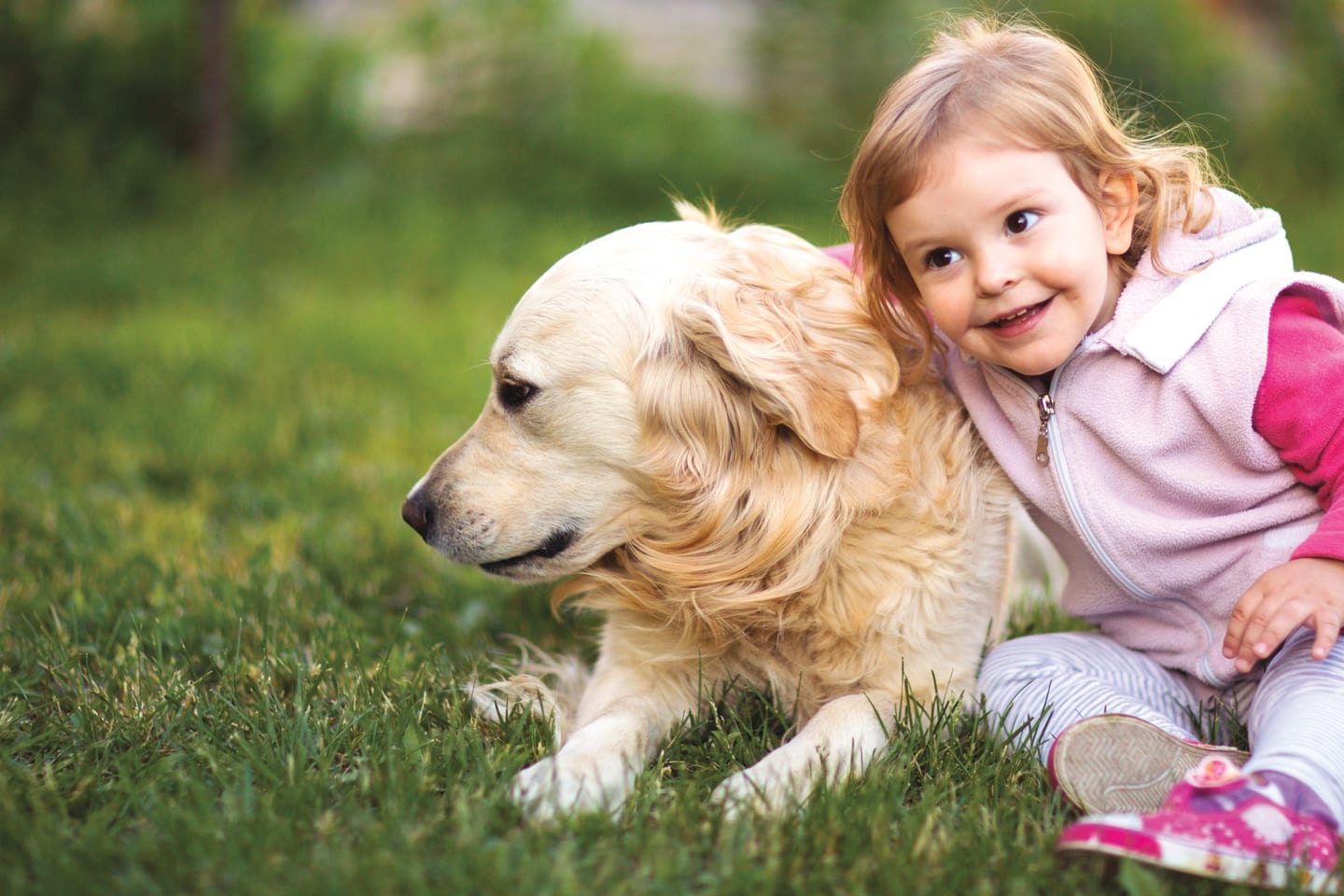 little girl sitting outside with her arm around a dog