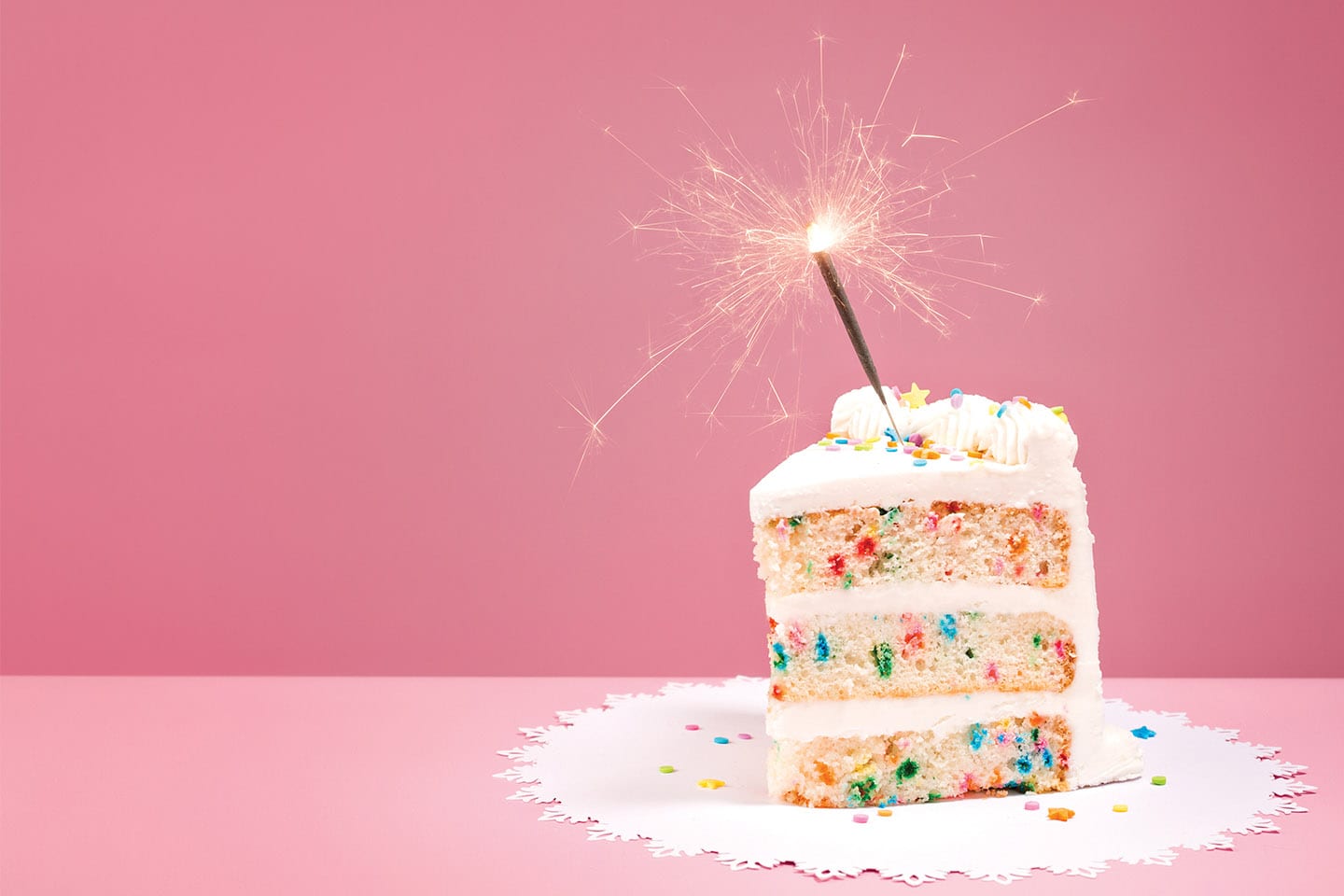 confetti birthday cake with sparkler candle on pink background in chattanooga