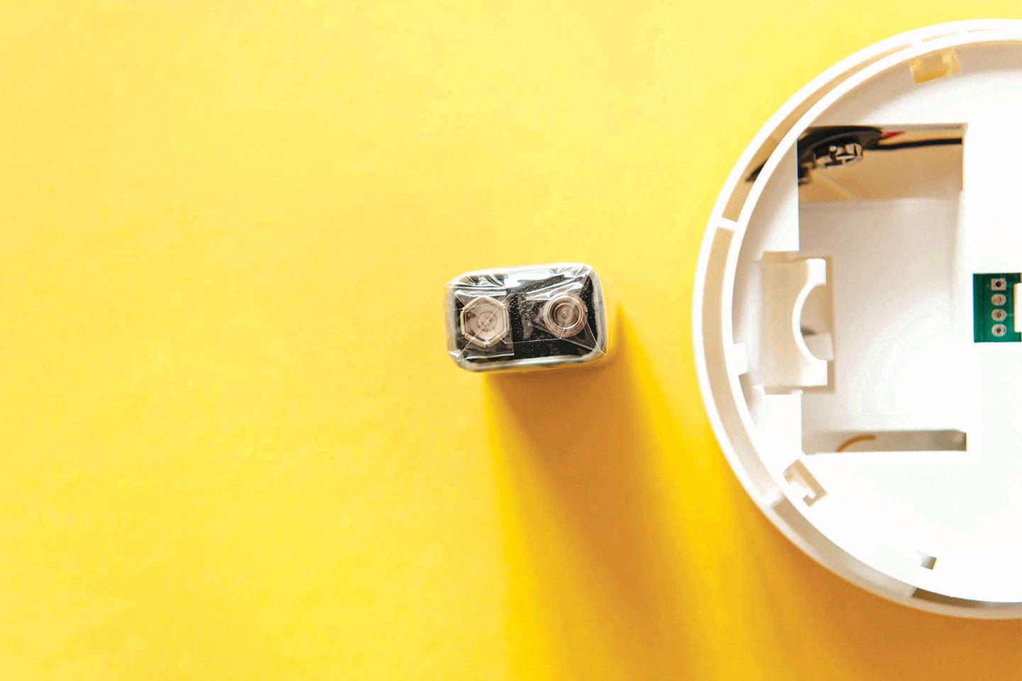 Smoke detector with 9 volt battery sitting next to it on yellow background in chattanooga