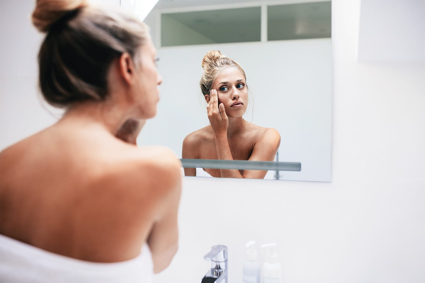 woman looking at skin on her face in bathroom mirror in chattanooga