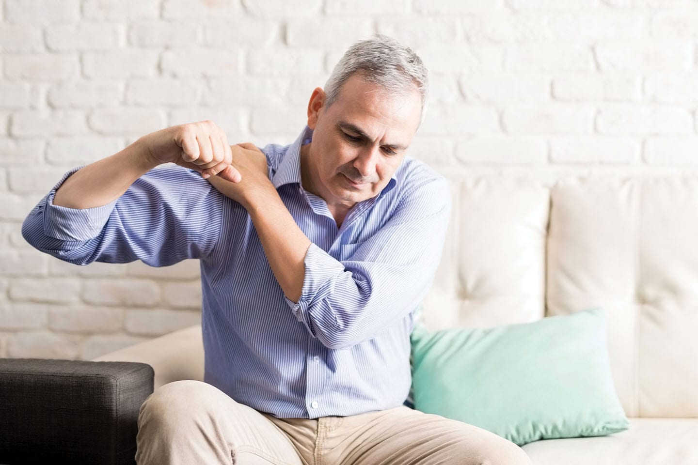 mature man rotating shoulder in pain on couch in chattanooga