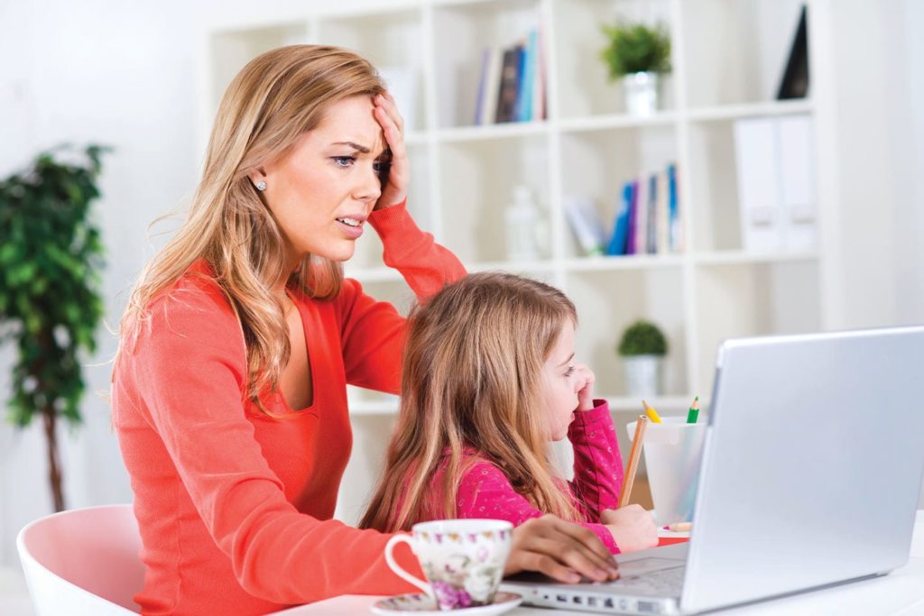 stressed out mother looking at comments on her computer whil her daughter sits in her lap mom shaming chattanooga