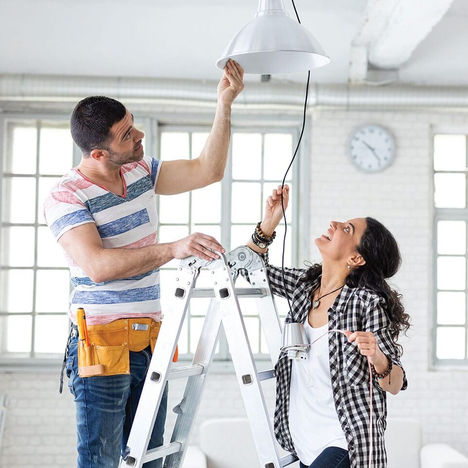 couple hanging a light fixture in their home they're remodelling without stress