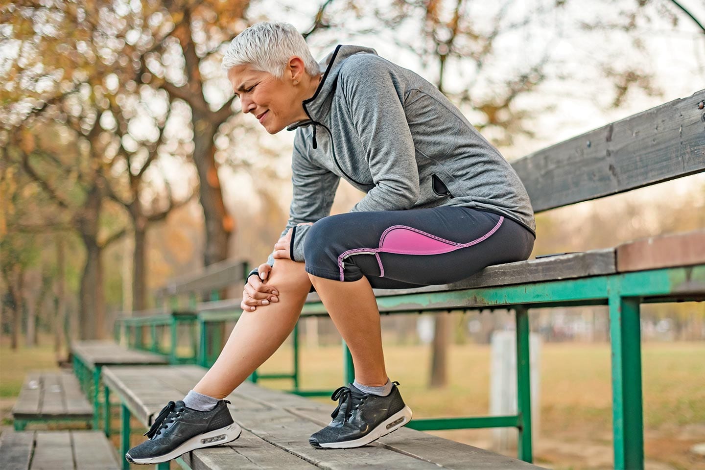 older woman with torn ACL sitting on park bench in pain holding knee