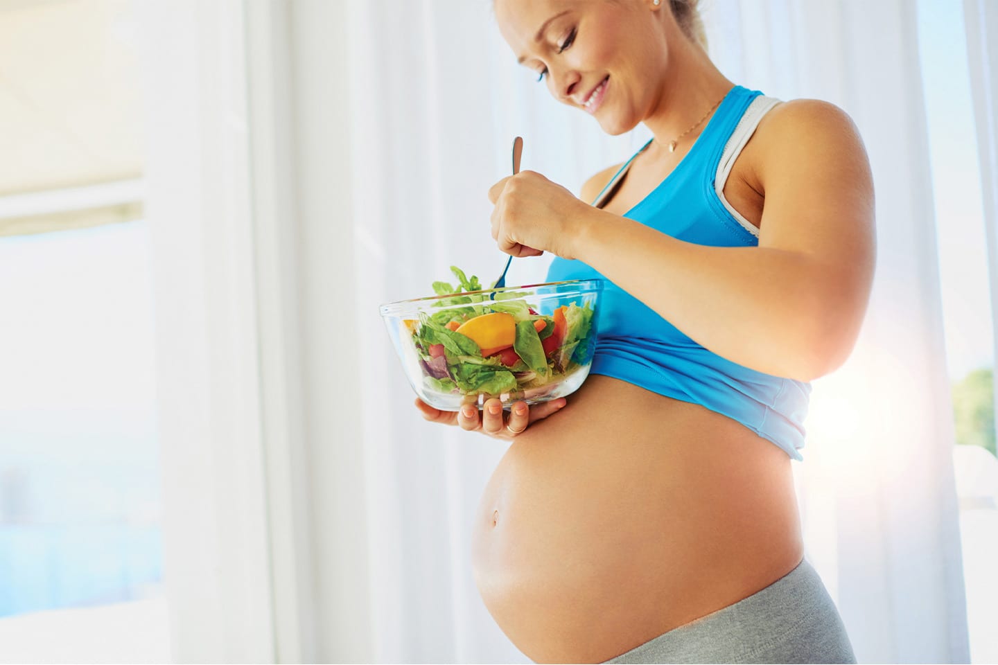 happy pregnant woman eating a salad after her workout