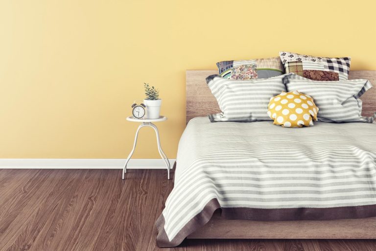 comfy bed with striped gray comforter in a room with yellow walls