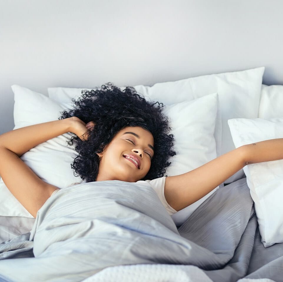woman smiling and stretching as she wakes up in the morning to start her day