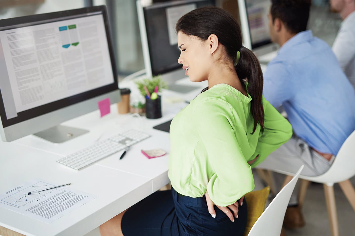 woman sitting at her computer desk at work with back pain