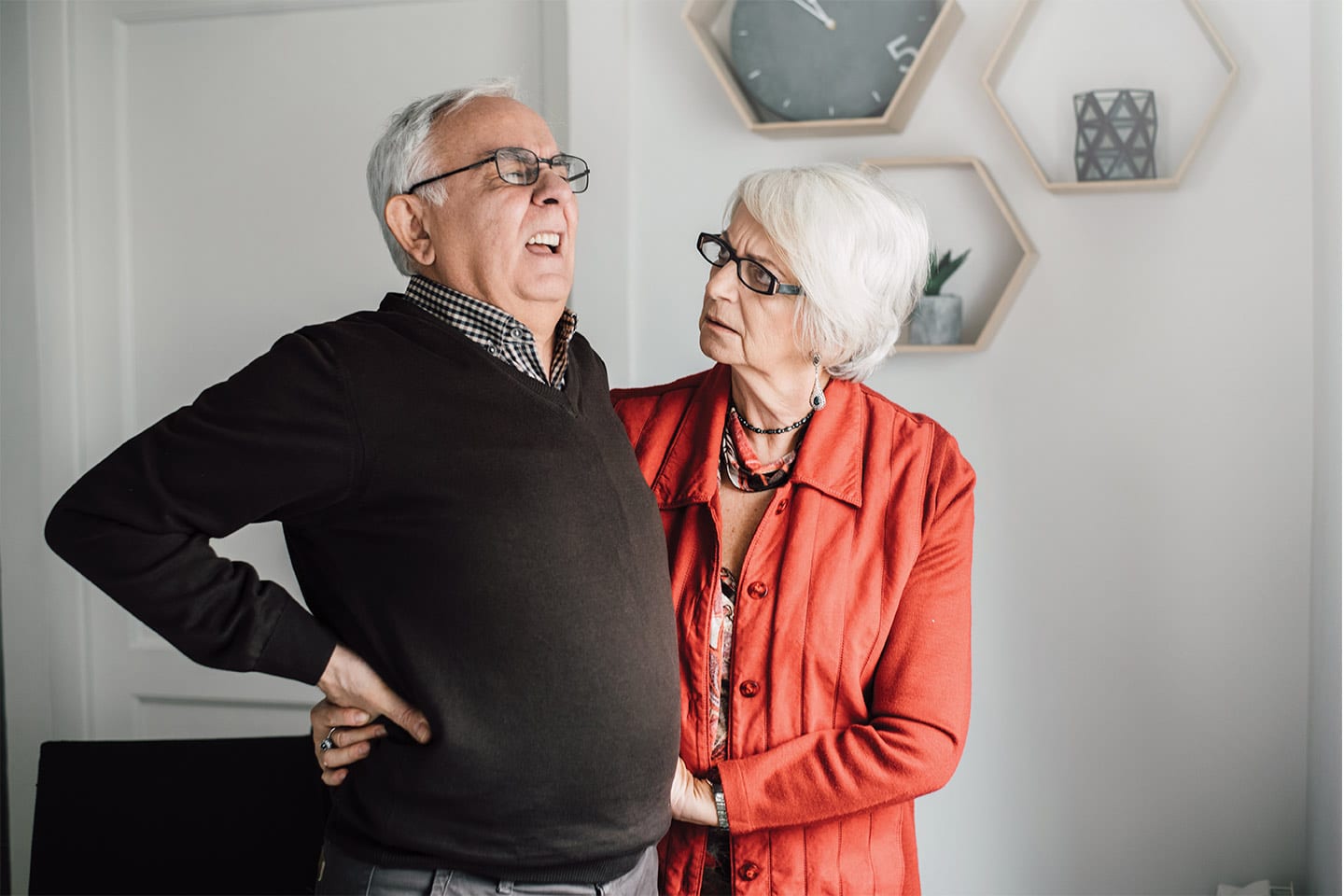 senior adult man with back pain and his concerned wife trying to help