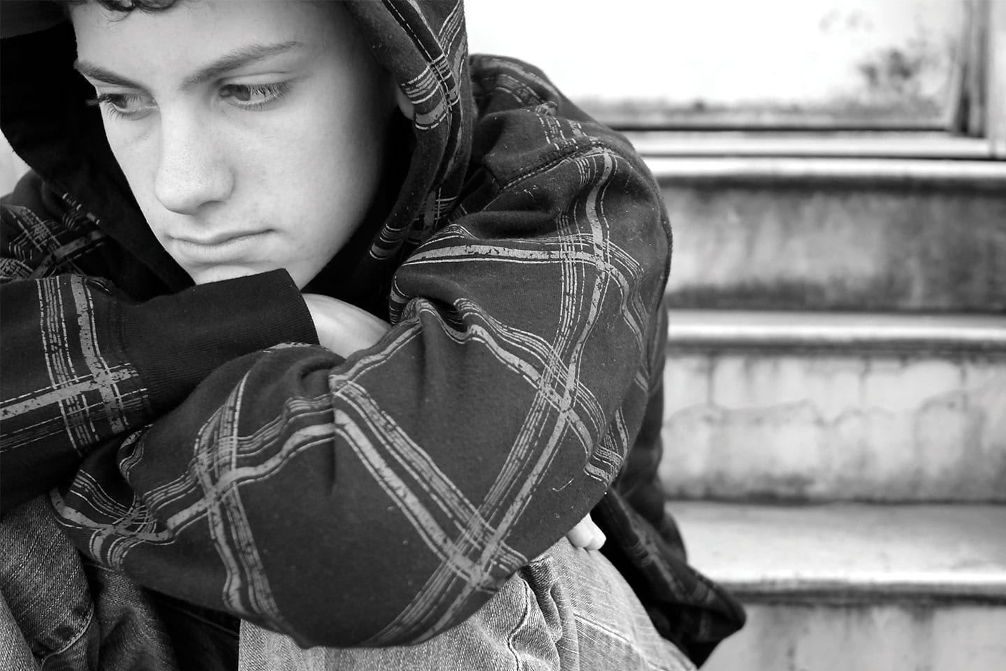 lonely and depressed teen boy sitting on steps wearing a hoodie