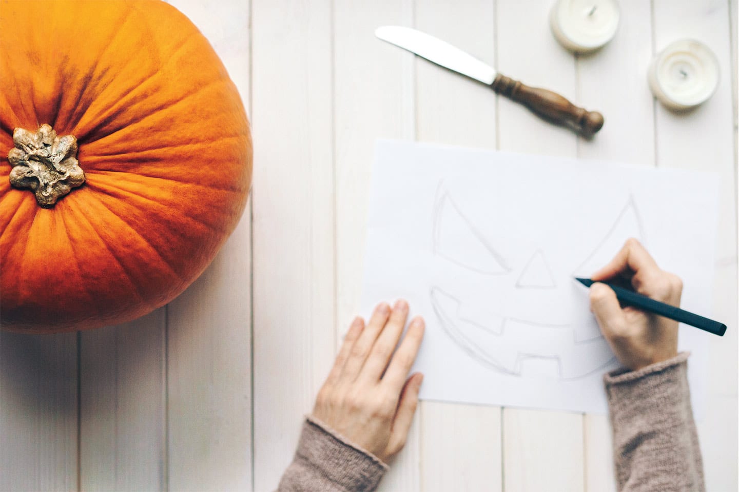 hands tracing a template for carving a jack-o-lantern pumpkin for halloween