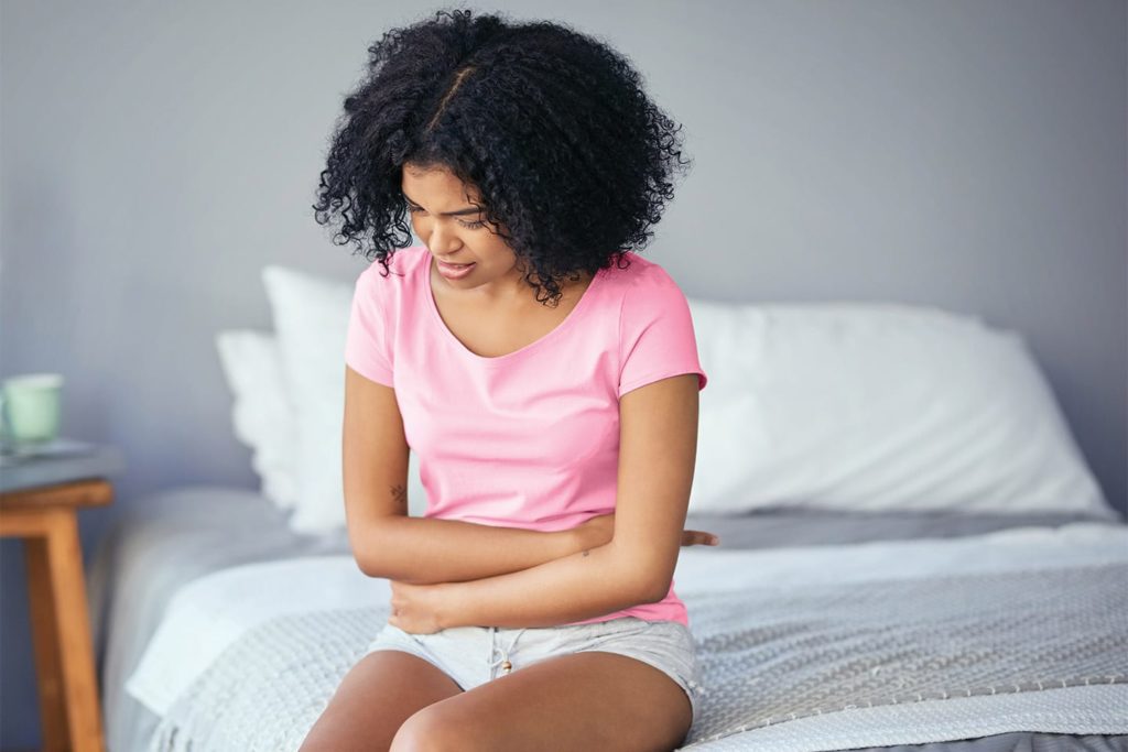 young woman sitting on bed with cramps from her pcos