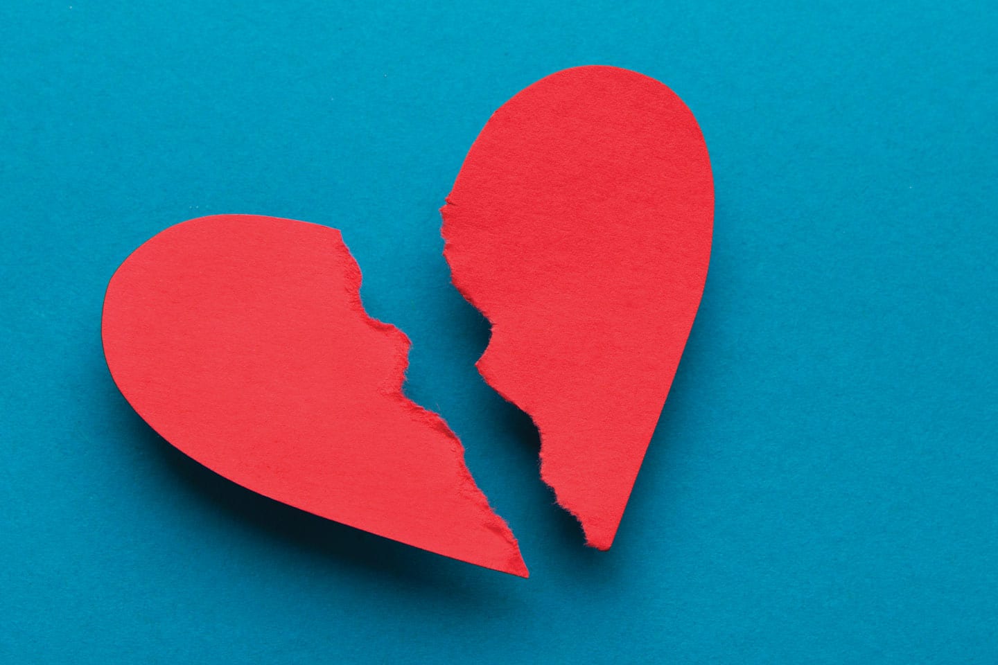 Torn red paper heart on a blue background representing a broken heart