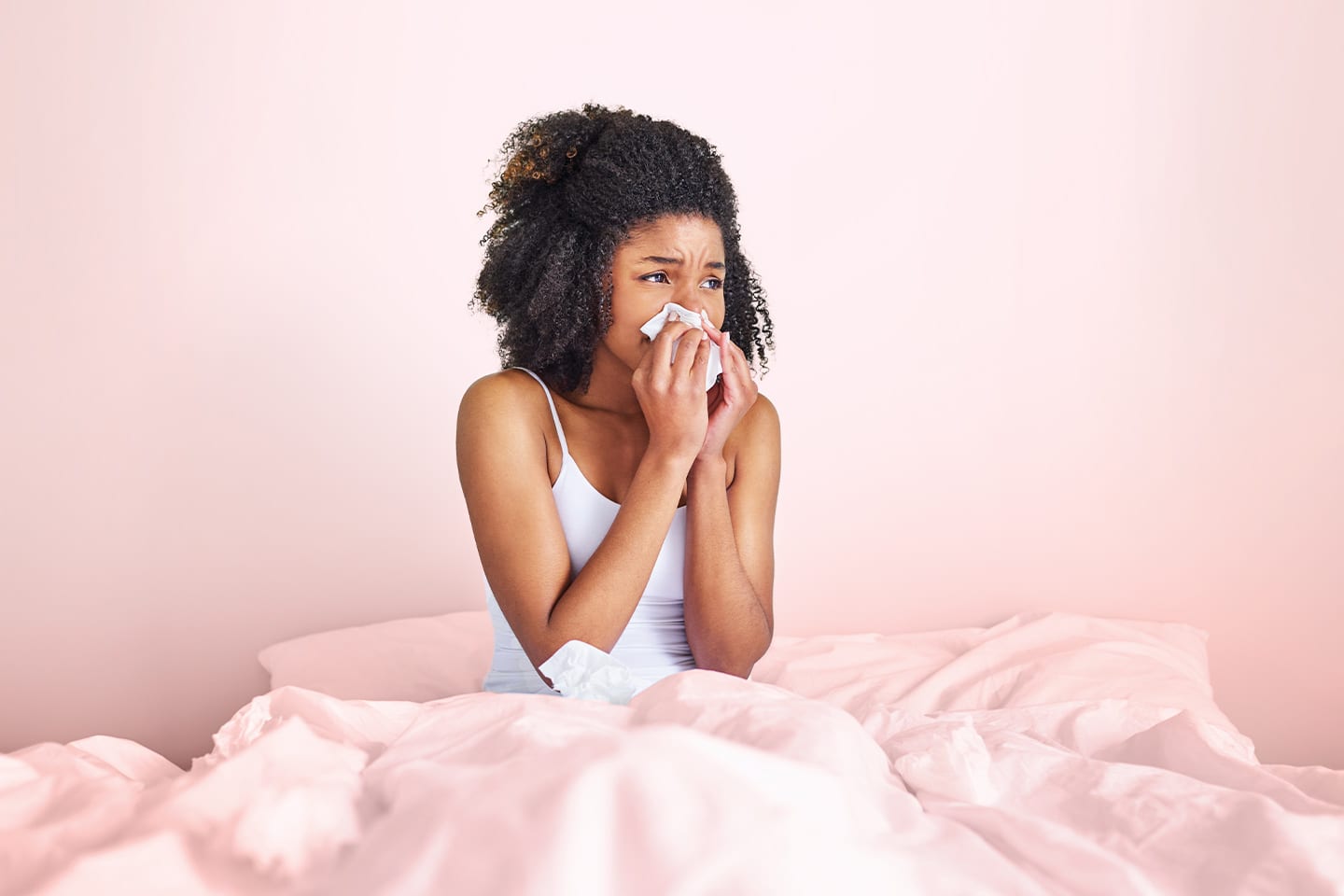young woman sitting in bed blowing her nose 