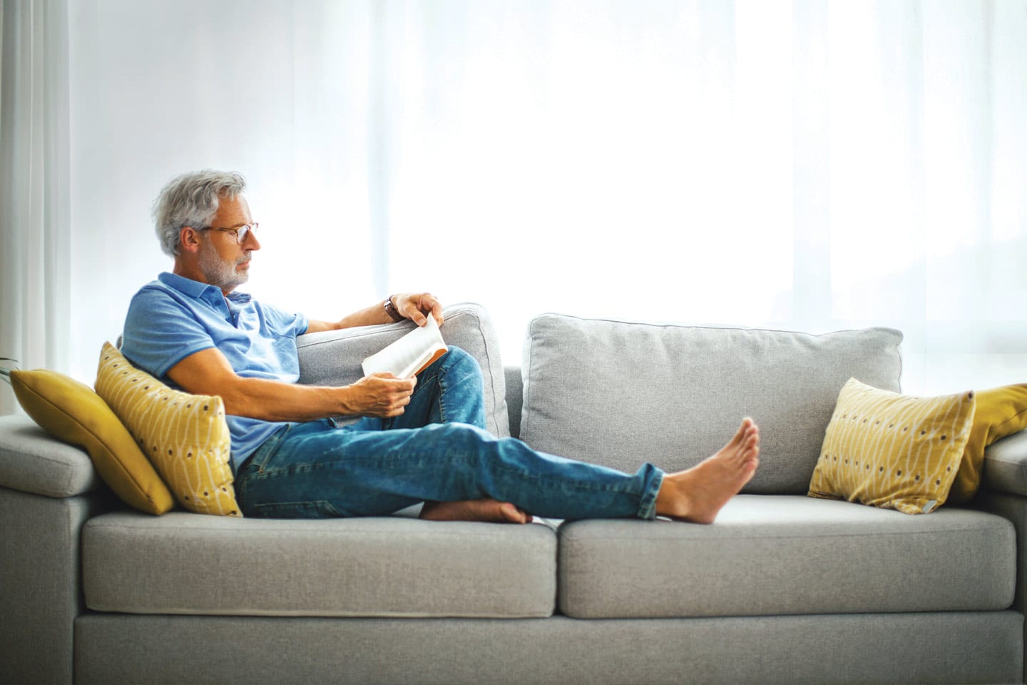 older man reading a book alone on the couch