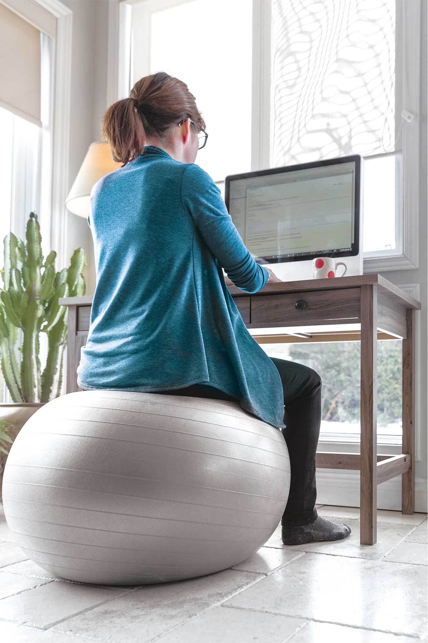 woman sitting on an exercise ball at her desk to help with posture