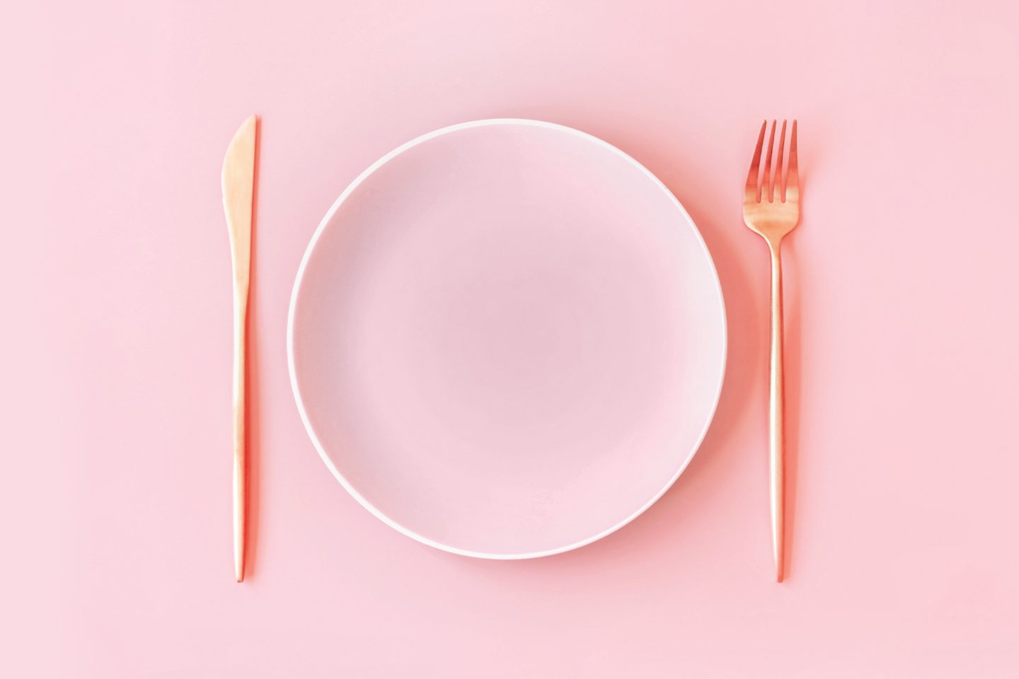 empty pink plate with rose gold utensils next to it