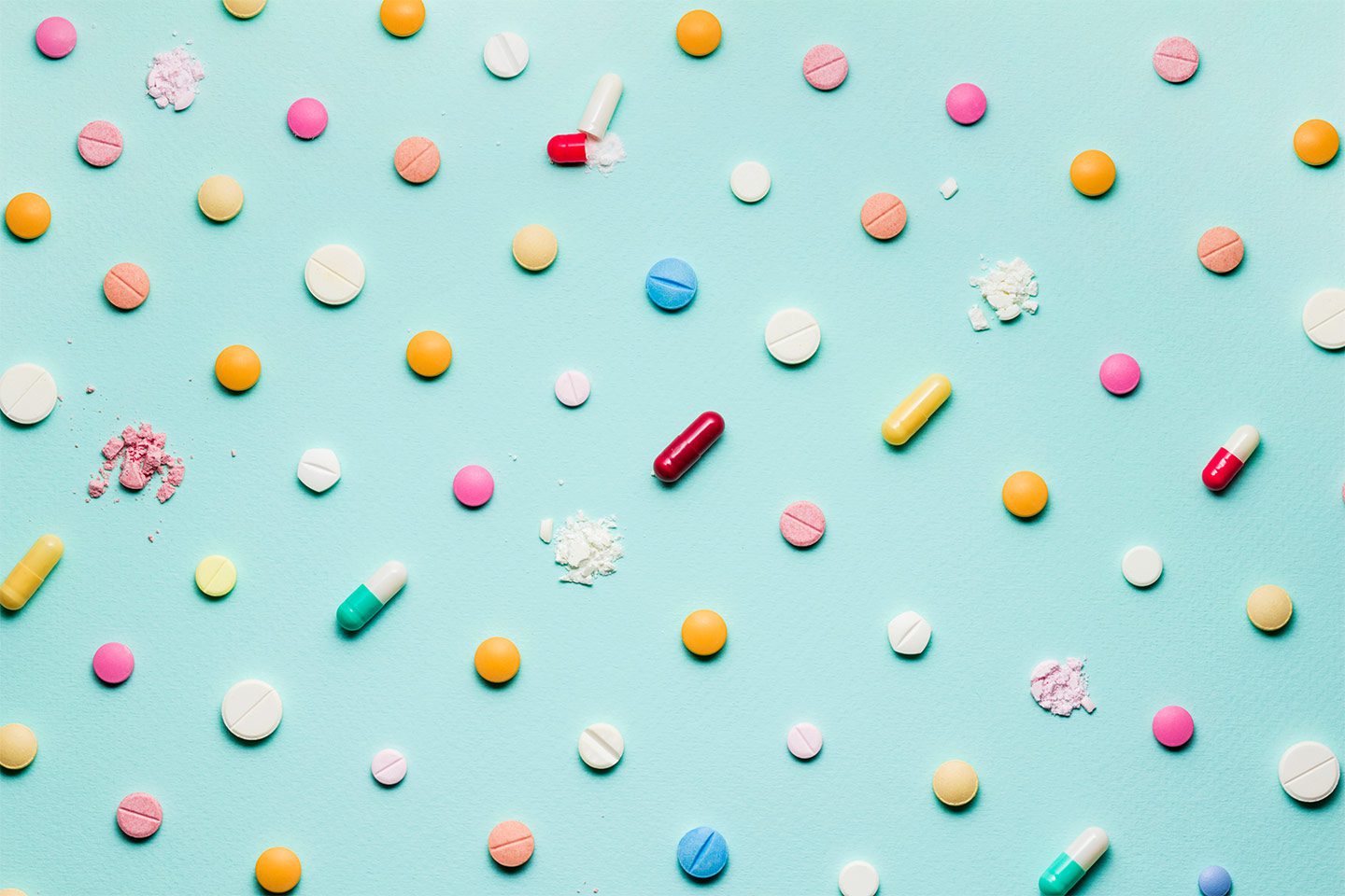 assorted colorful crushed pills and vitamins on a light blue background