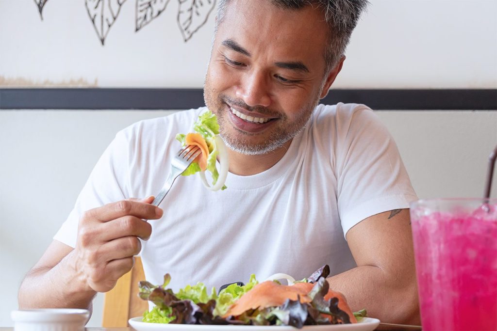 smiling man eating a salad with smoked salmon on it