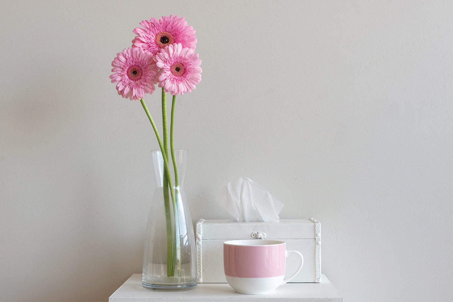 flowers on a night stand with a mug of tea and a tissue box