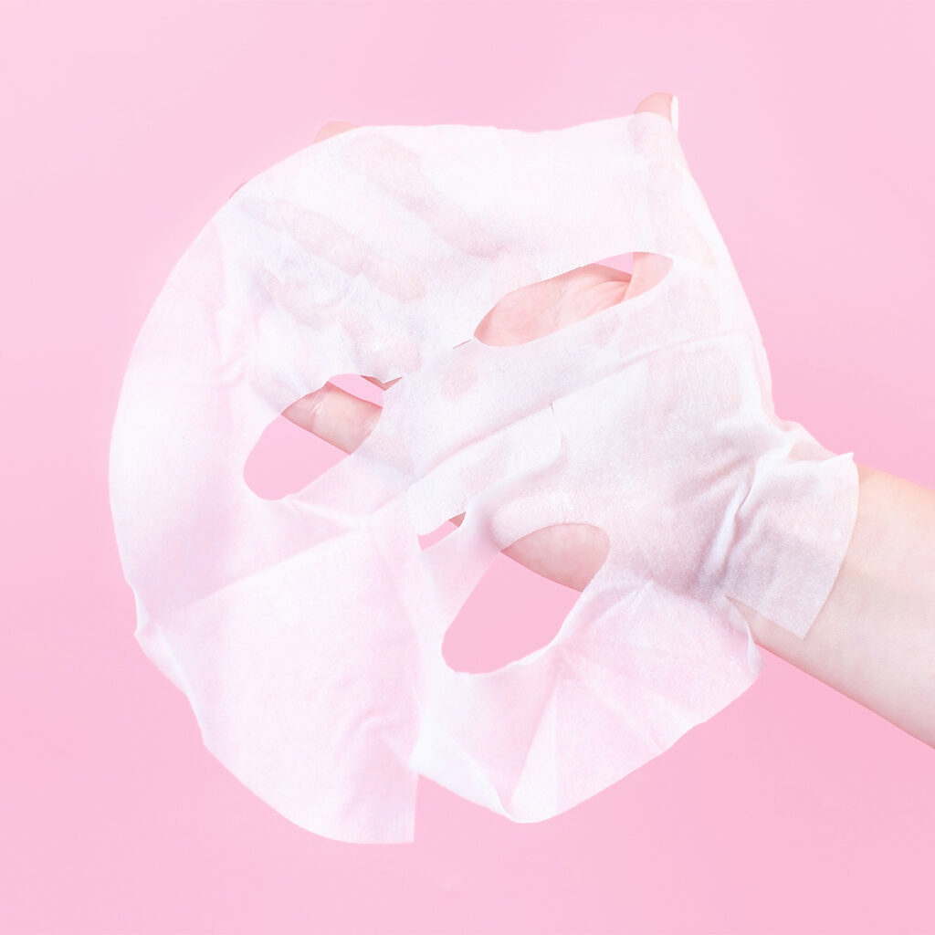 woman holding a thin sheet mask in pink background