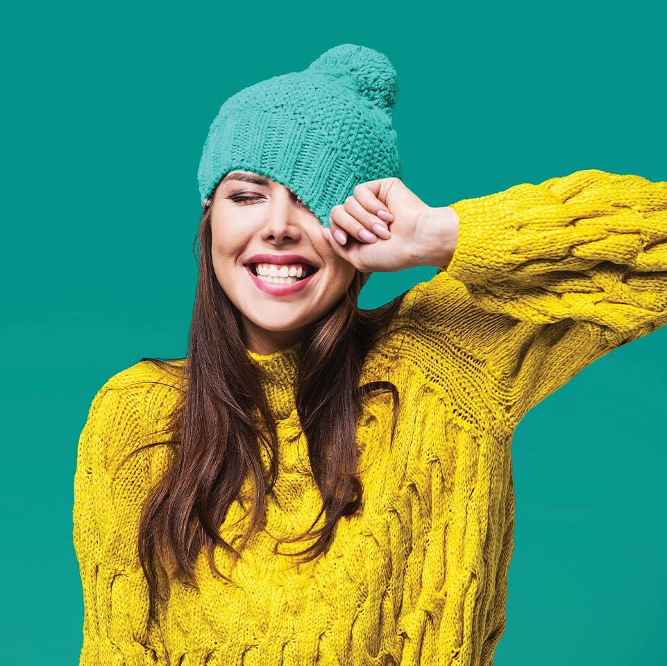 happy young woman in yellow sweater pulling a toboggan over her hair