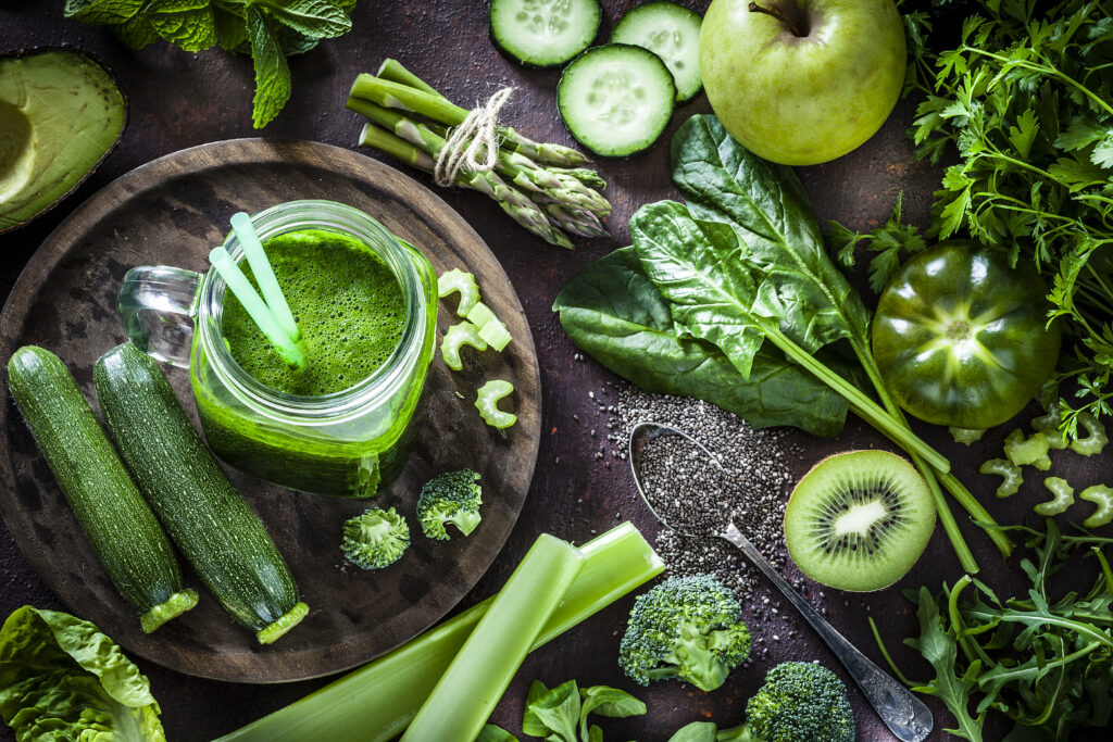 A vibrant assortment of green fruits and vegetables, including cucumbers, celery, apples, and leafy greens artistically arranged.