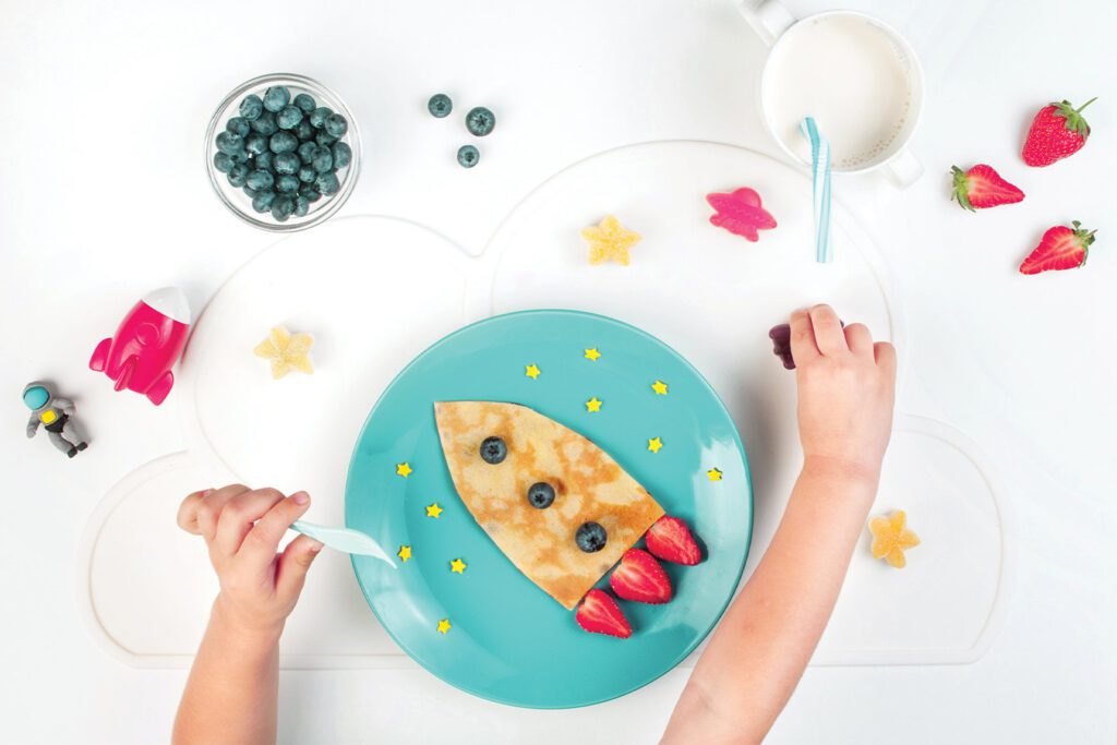 little boy eating pancakes shaped like a rocket ship