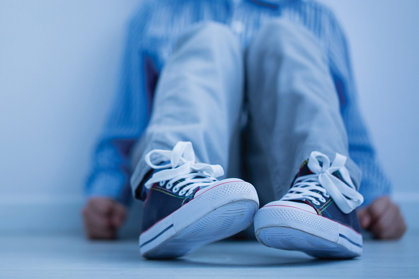 boy with autism wearing converse sitting against the wall