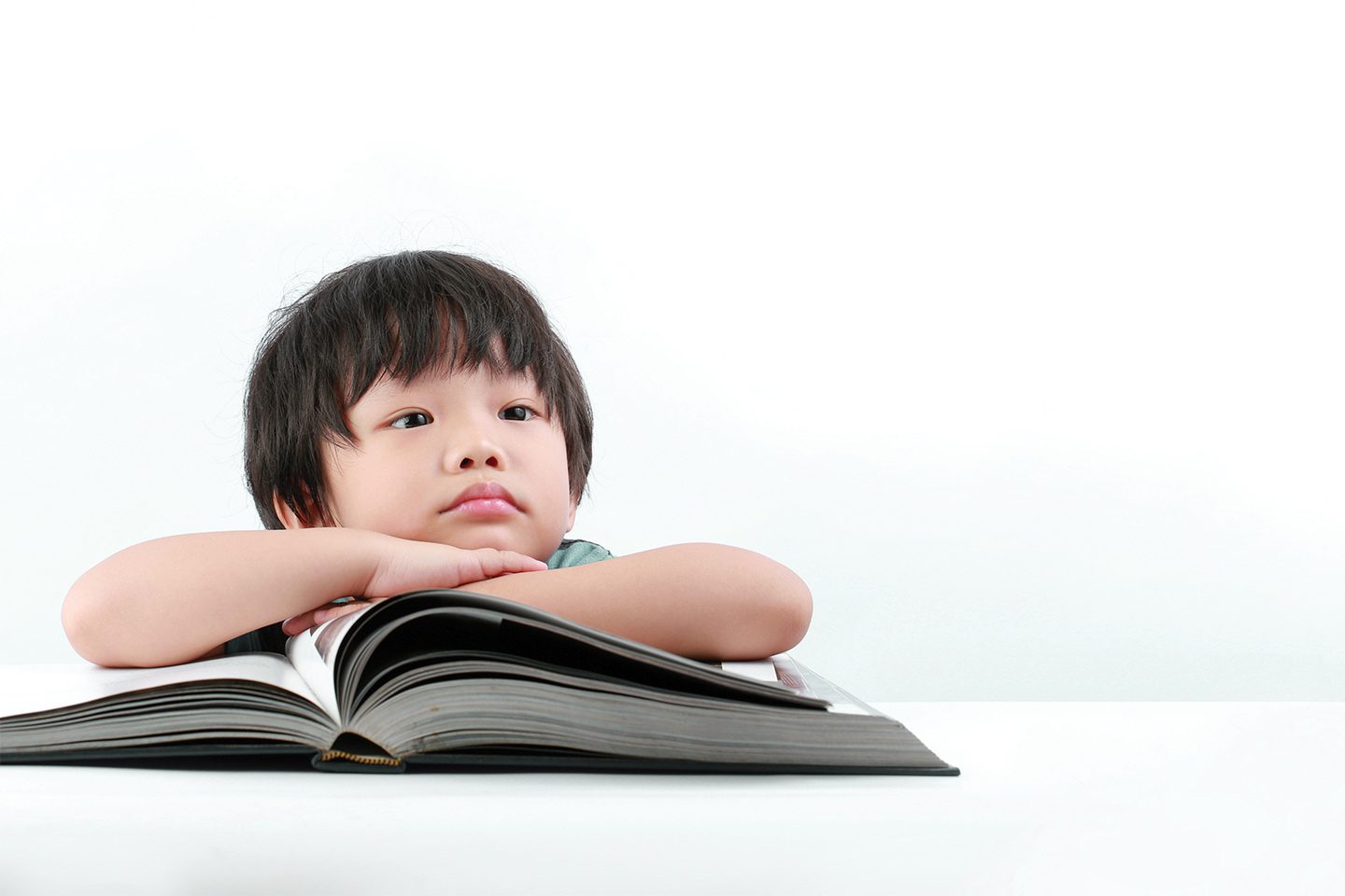 Young boy with arms folded over a large book.