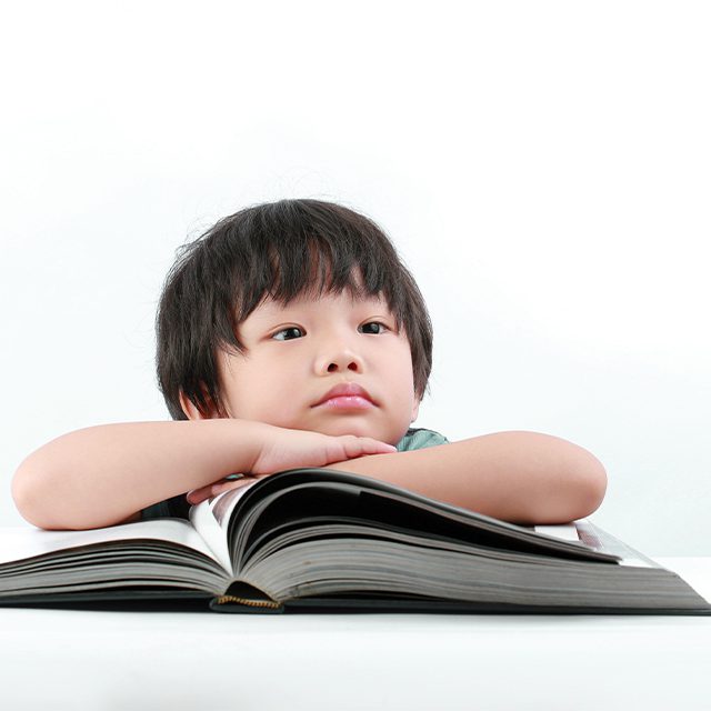 Boy with arms crossed over a large book.