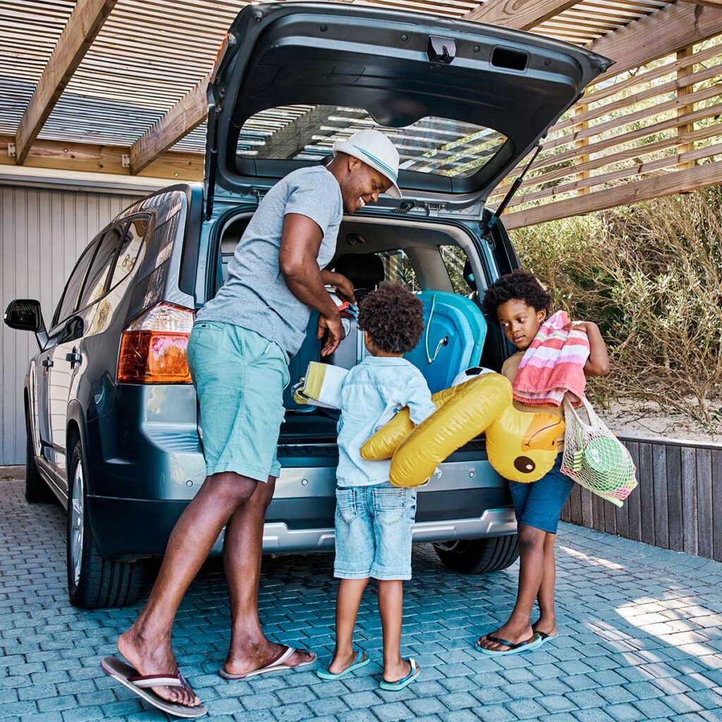 Father packing things in his car trunk with his two kids for summer vacation