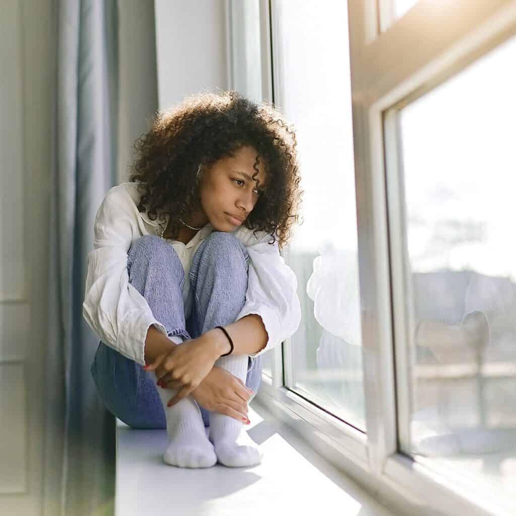 stress and anxiety | depressed woman sitting on a window sill