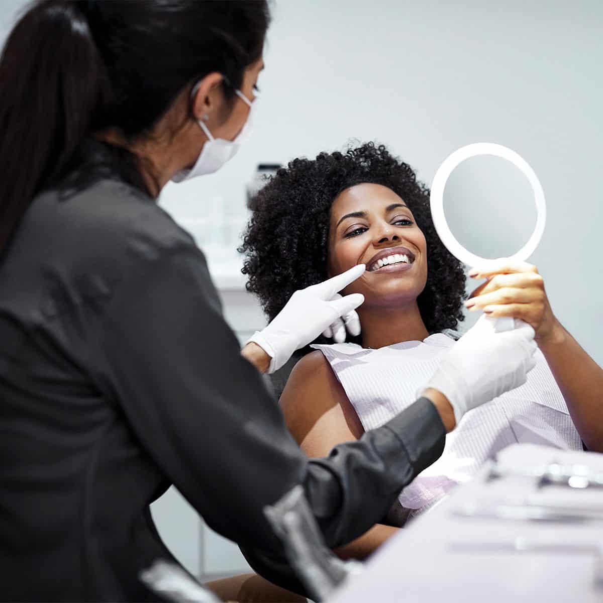 female dentist handing her patient a mirror to look at her teeth