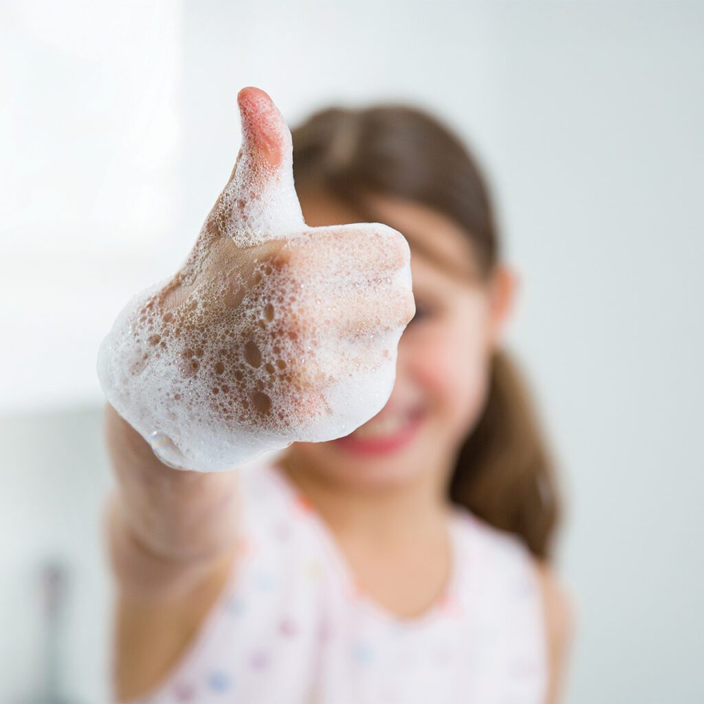 girl with bubbles on her hand putting her thumbs up